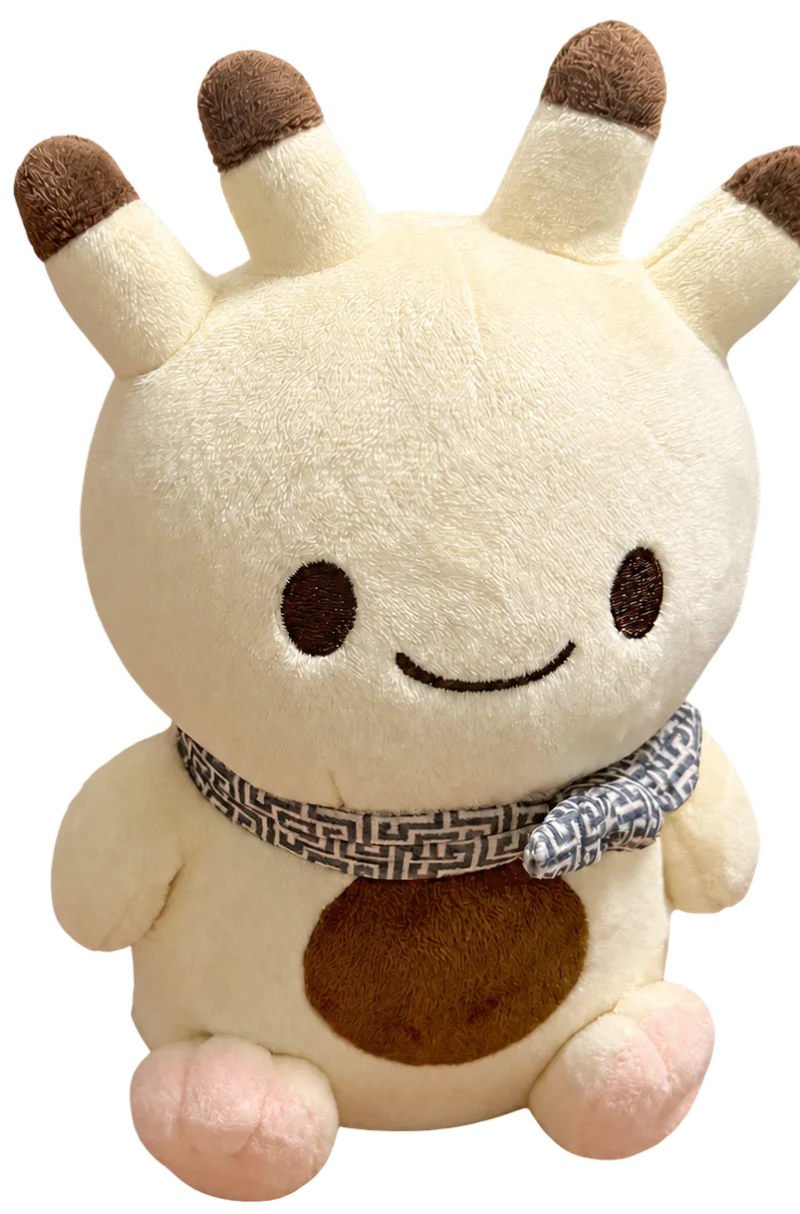 クリーム色の毛と先が茶色いツノを持つナンダモンのぬいぐるみ。柄入りの首巻きを巻き、茶色いおなかで座っている。