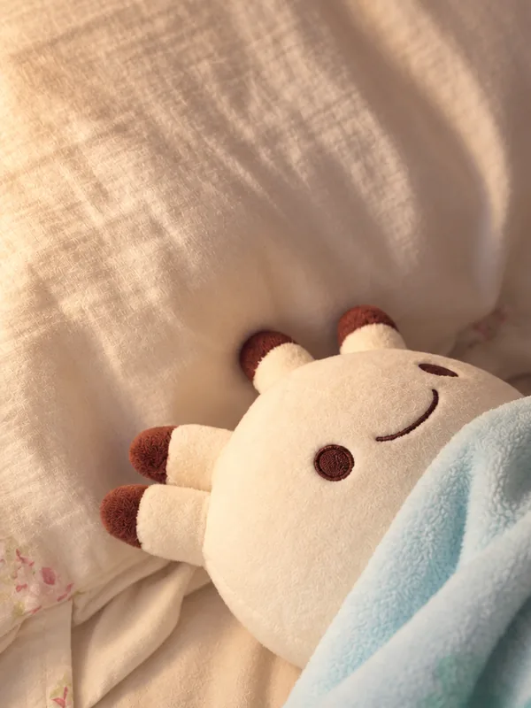 枕に頭をのせ、水色の毛布をかけて眠るナンダモンのぬいぐるみ。